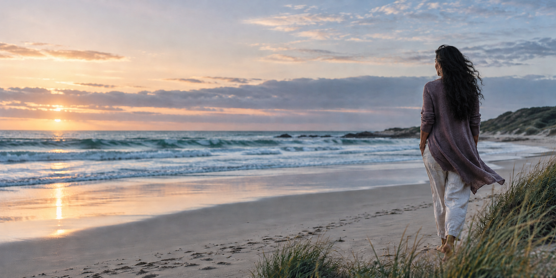 A woman walking along a calm shoreline at sunrise